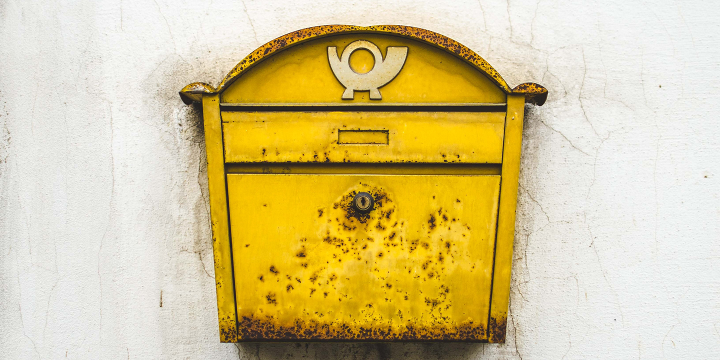 Gelber rostiger Briefkasten an einer Wand.