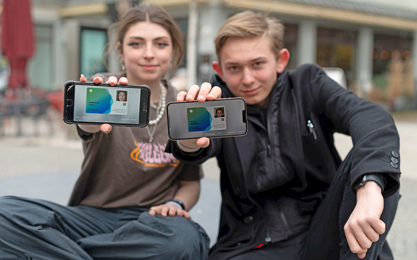 Zwei Jugendliche sitzen in Dornbirn am Marktplatz und strecken ihre aha App am Smartphone in die Kamera
